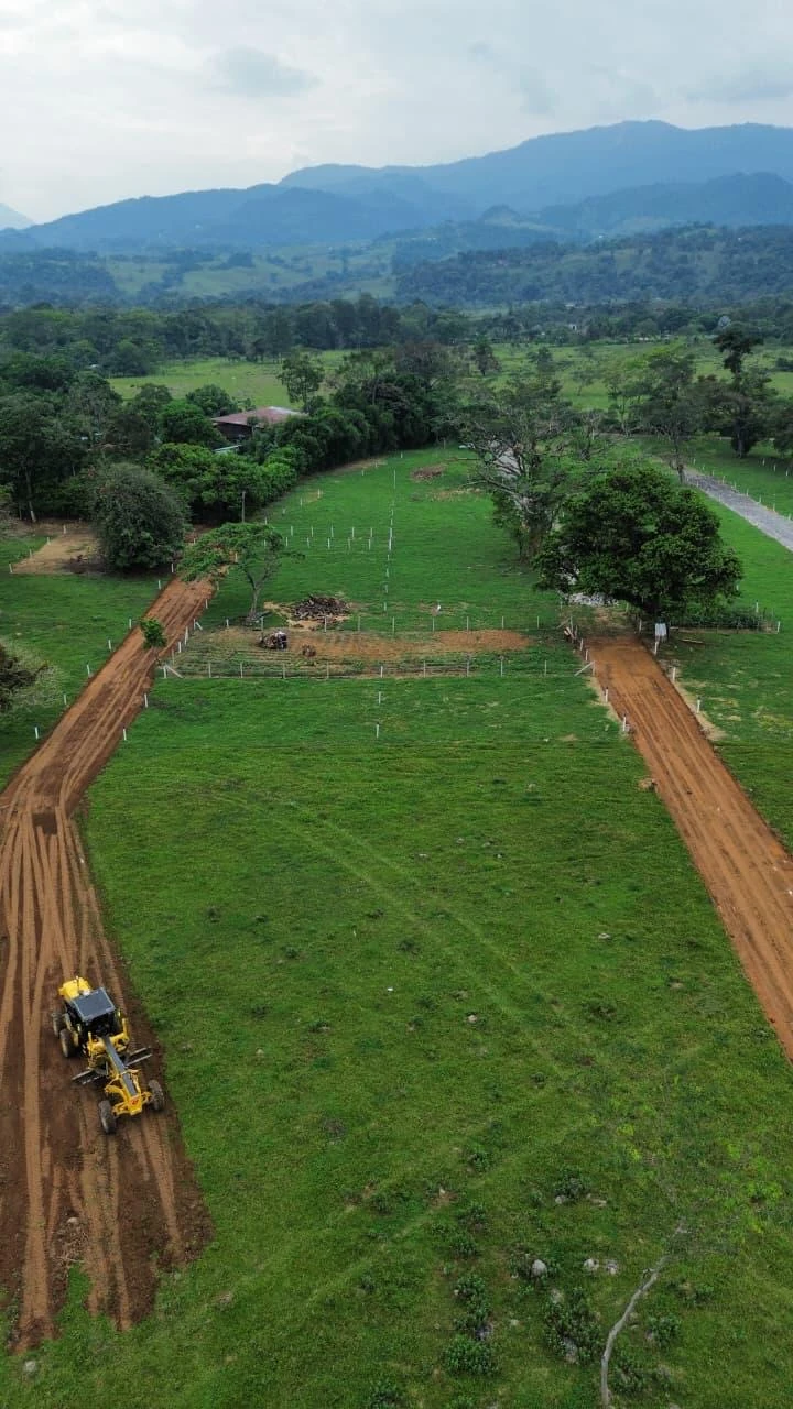 Proyecto de lotes en desarrollo con caminos de tierra, lote demarcado y montañas al fondo